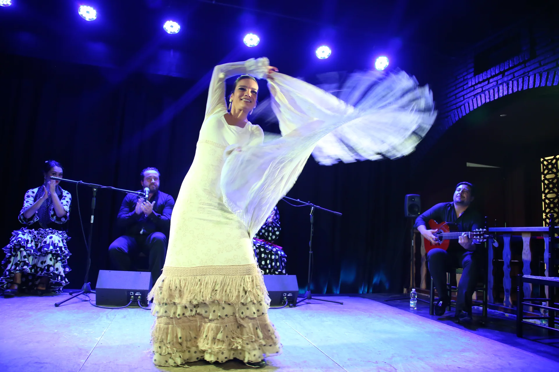 Flamenková tanečnice v piruetě na pódiu tablaa, cuadro se zpěvákem a kytaristou po obou stranách
